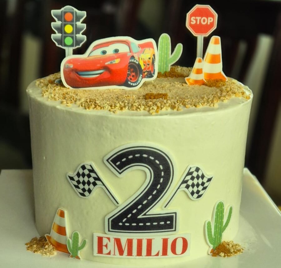 Pastel infantil personalizado temático de Cars con el número 2, nombre Emilio y decoraciones de carreteras, conos y Rayo McQueen.